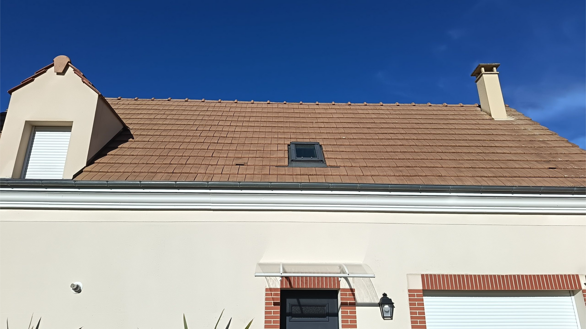 Maison beige avec un toit de tuiles en terre cuite et un ciel bleu en arrière-plan.