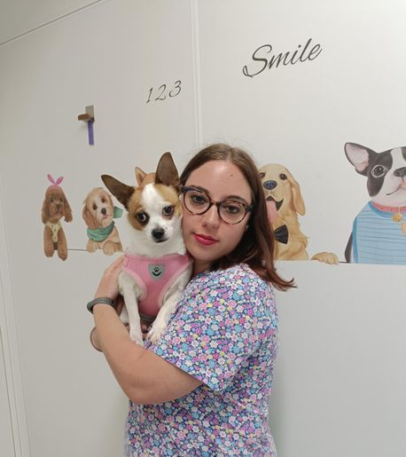 Mujer con gafas sostiene un perro pequeño frente a una pared con decoración con temática de perros.