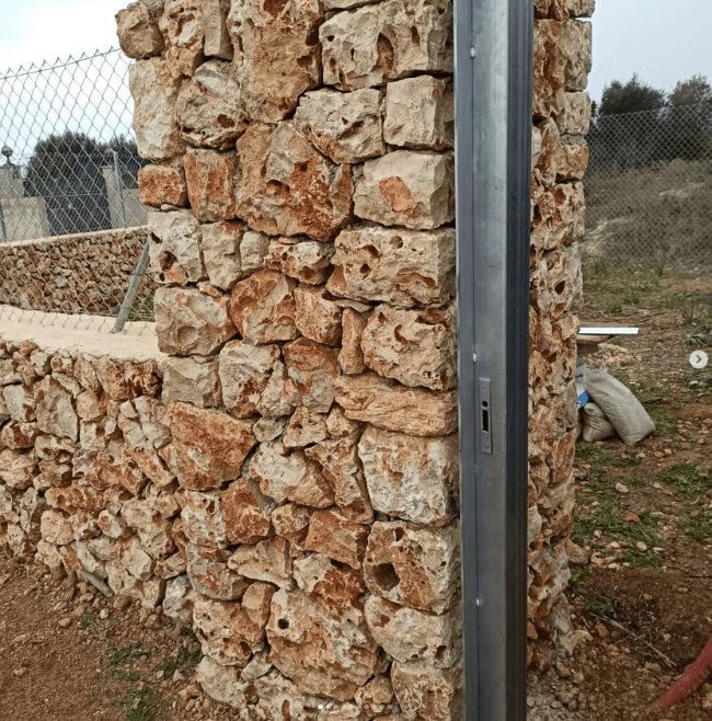Un muro de piedra con un poste de metal delante.
