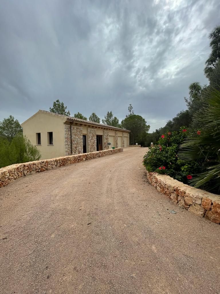 Un camino de tierra que conduce a una casa con un muro de piedra.