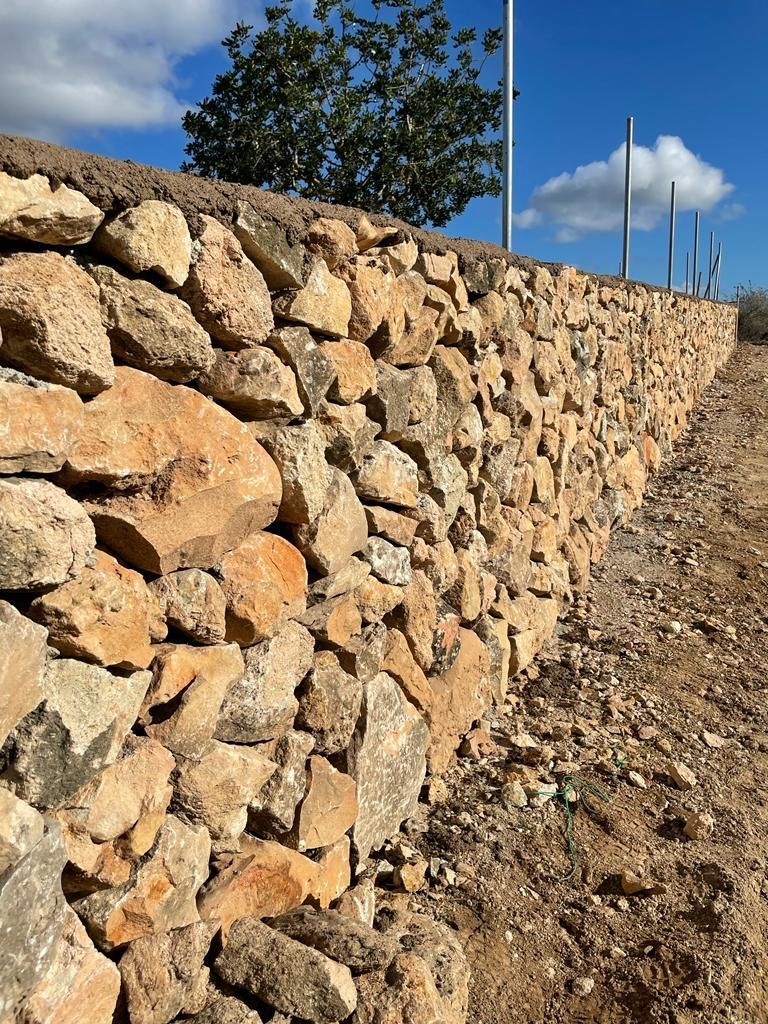 Un muro de piedra a lo largo de un camino de tierra con un cielo azul al fondo.