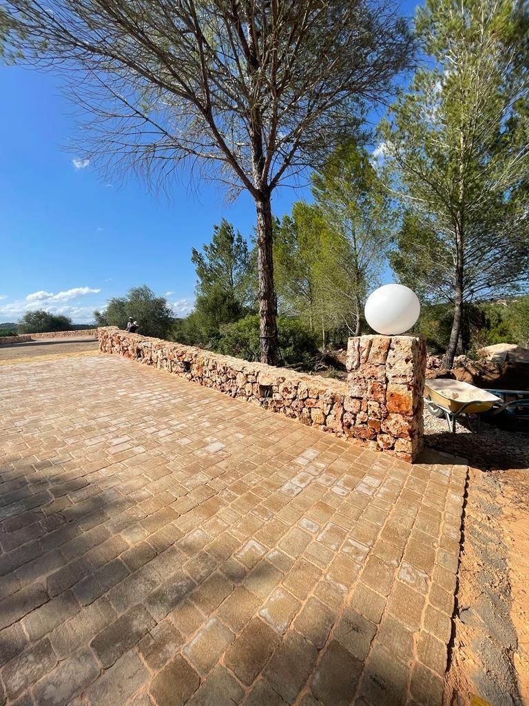 Una pasarela de ladrillo con un muro de piedra y árboles al fondo.