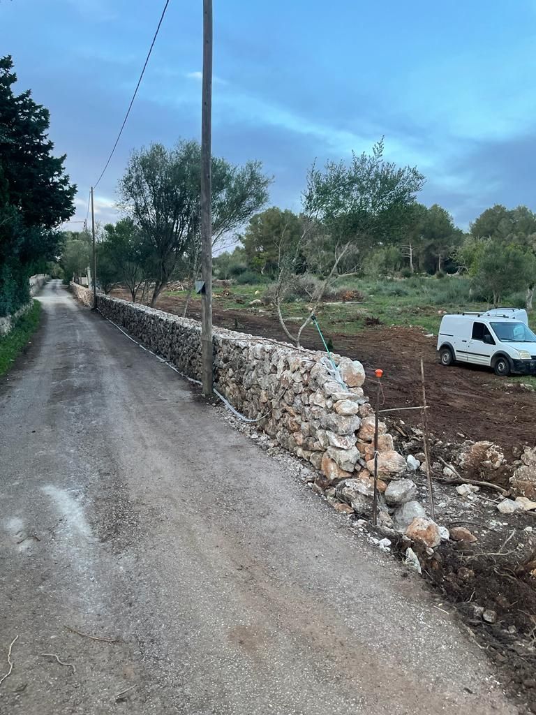 Una camioneta blanca está estacionada al costado de un camino de tierra al lado de un muro de piedra.