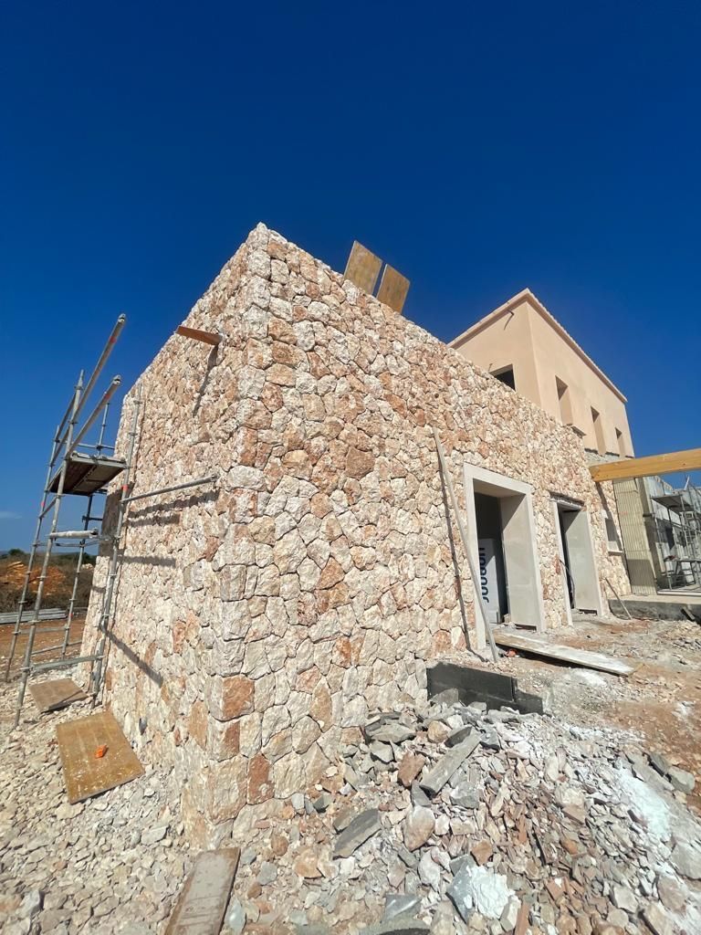 Se está construyendo un gran edificio de piedra con andamios y un cielo azul al fondo.