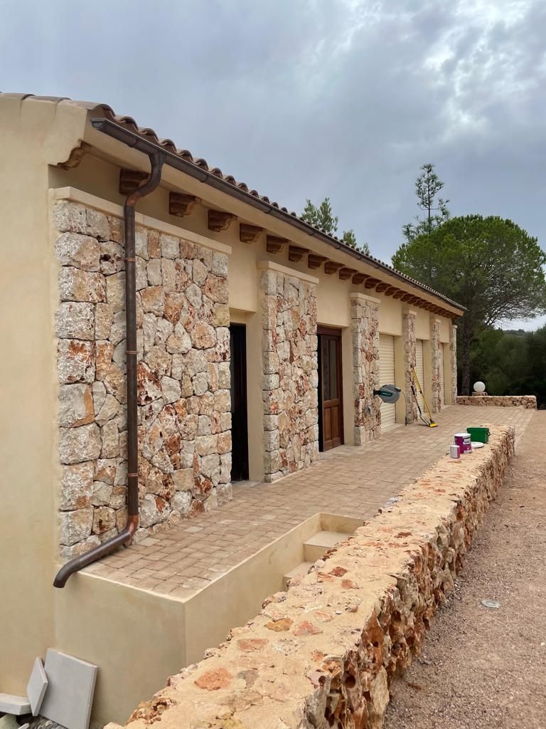 Una casa con un muro de piedra y un canalón al costado