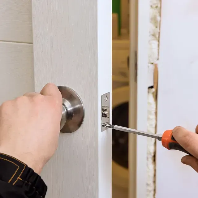 Una persona está instalando un pomo de puerta con un destornillador.
