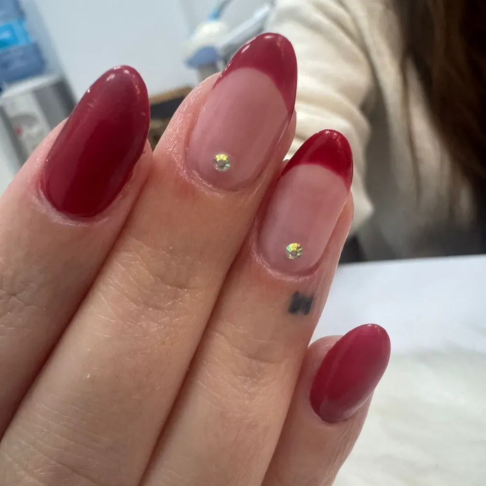 Mano con uñas de punta roja y francesa, una de ellas con pequeña gema.