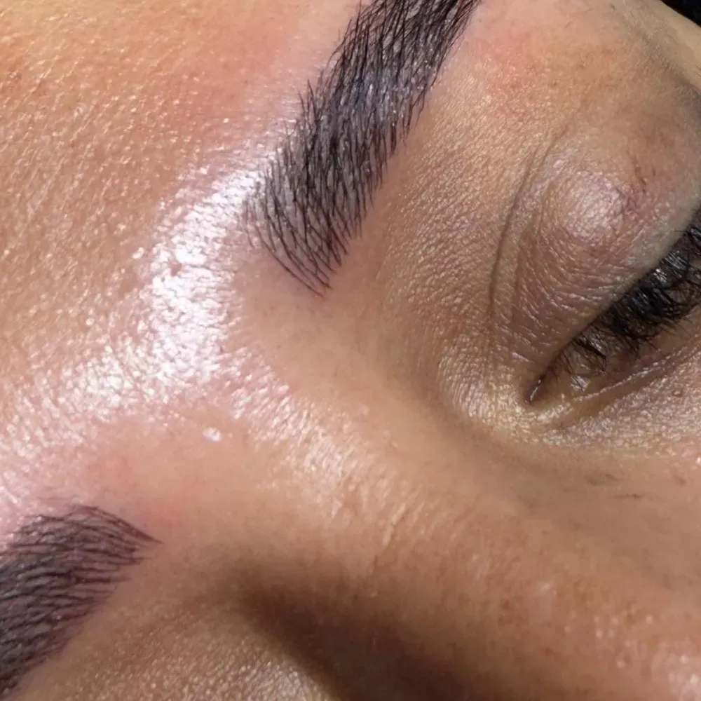 Primer plano de las cejas de una persona después del microblading, la piel está ligeramente grasosa, ojos cerrados.