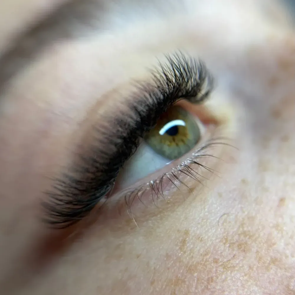 Primer plano de un ojo con pestañas largas y oscuras e iris verde claro. La piel presenta pecas.