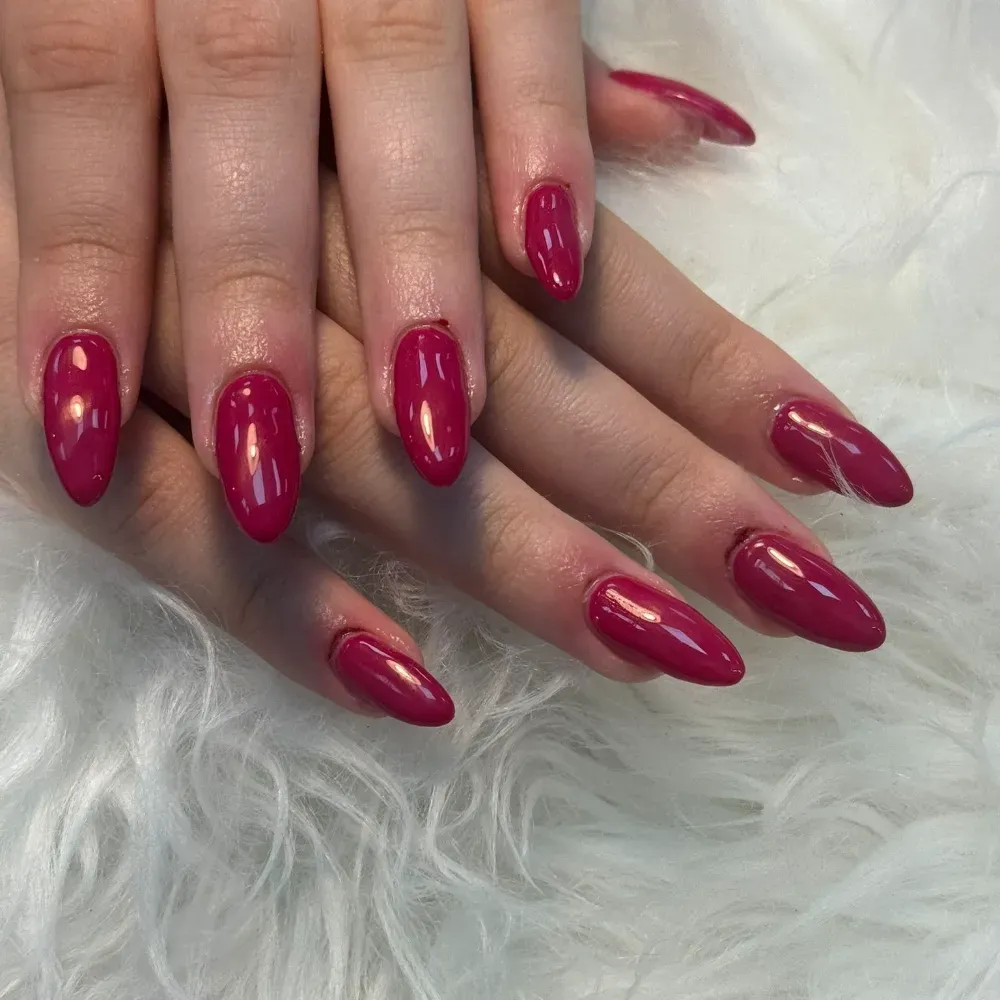 Manos con uñas en forma de almendra pintadas de un rosa oscuro brillante, que descansan sobre una superficie blanca esponjosa.