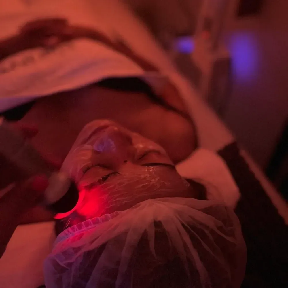 Persona recibiendo un tratamiento facial, acostada con terapia de luz roja.
