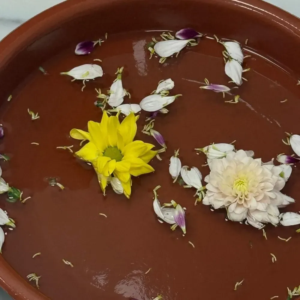 Cuenco marrón con flores y pétalos flotantes de color amarillo y blanco.