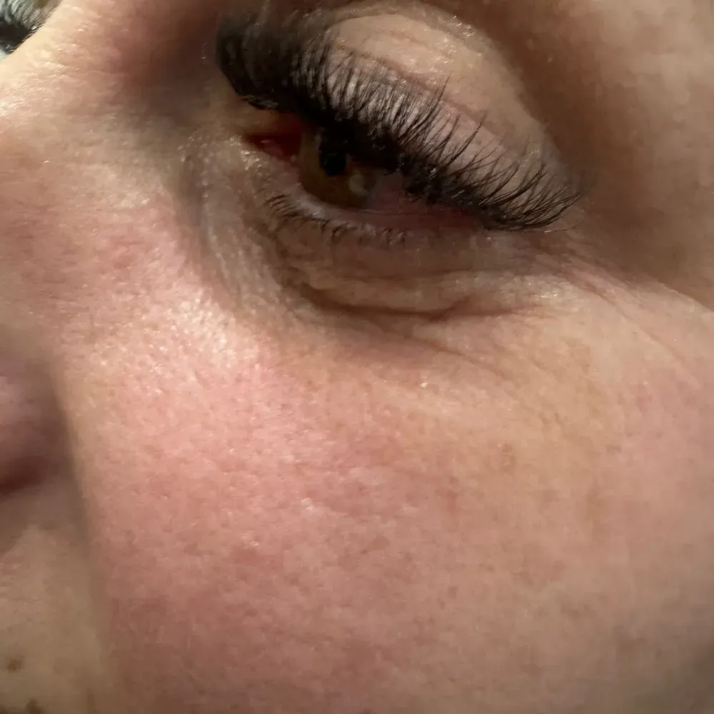 Primer plano del ojo de una persona con pestañas postizas oscuras y gruesas. La piel presenta líneas de expresión y pecas.