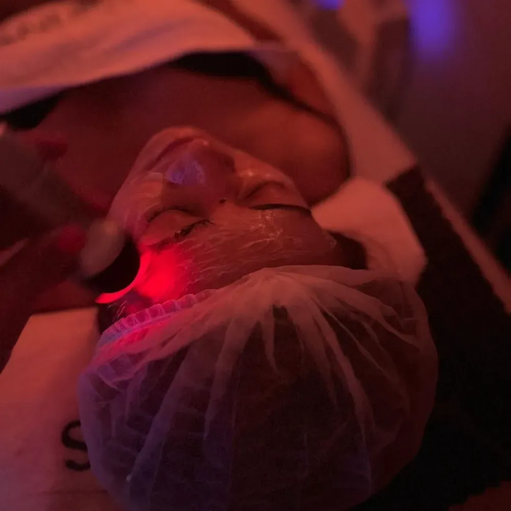 Persona que recibe un tratamiento facial con un dispositivo de luz roja en un spa.