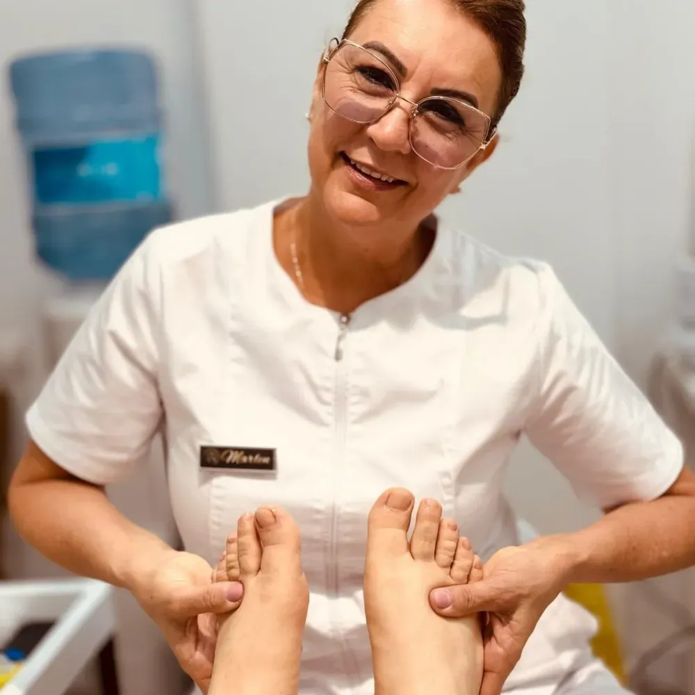 Persona con uniforme blanco, sosteniendo y examinando los pies de un cliente, probablemente en un spa o entorno médico.