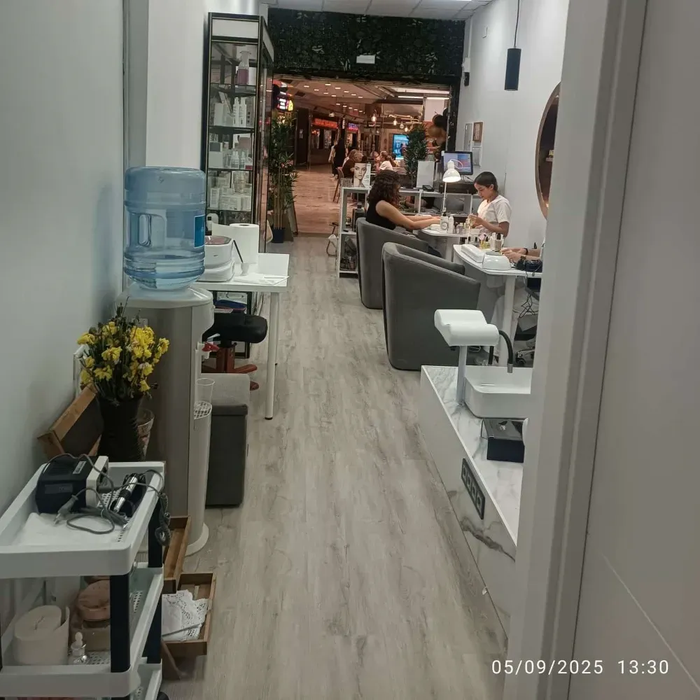 Interior de salón de uñas con clientes, un dispensador de agua y estaciones de uñas.