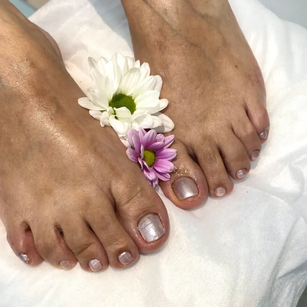 Pies con esmalte de uñas rosa claro, decorados con flores sobre tela blanca.