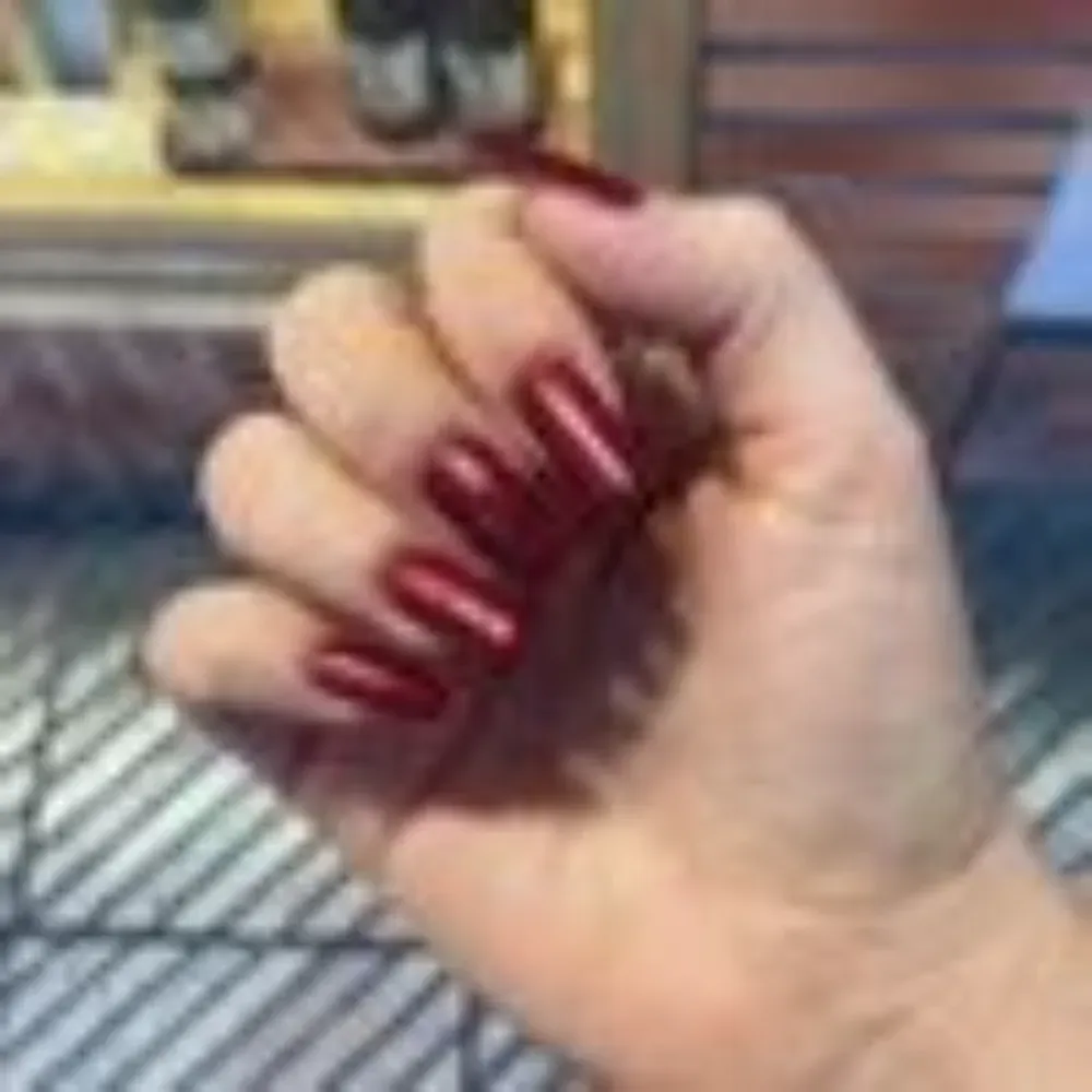 Mano con uñas largas, brillantes y de color rojo oscuro, posada sobre una superficie.