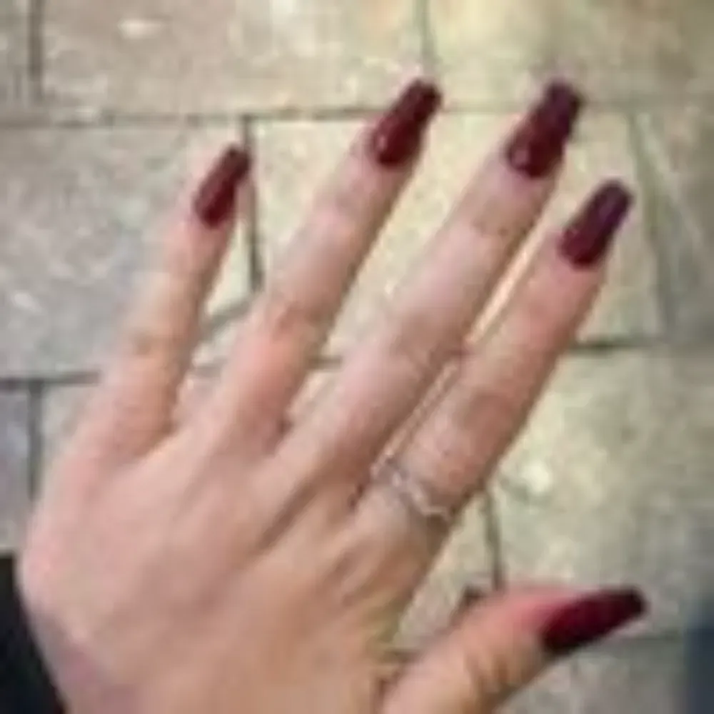 Mano con uñas largas, cuadradas, de color rojo oscuro y un anillo de plata en un dedo.