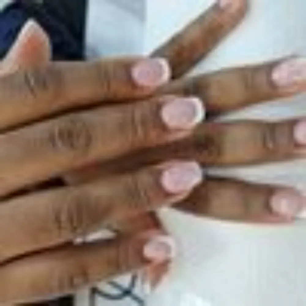 Manos con esmalte de uñas rosa y puntas blancas.