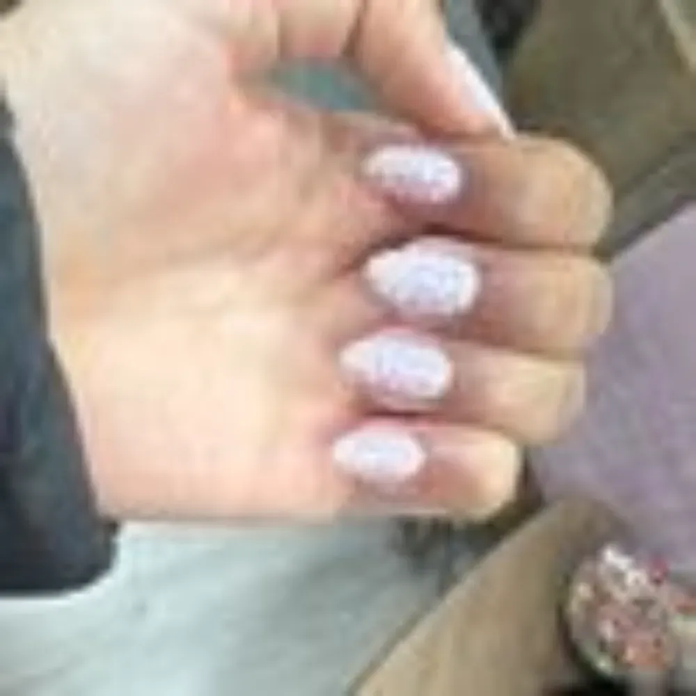 Mano con esmalte de uñas rosa claro con brillo blanco.