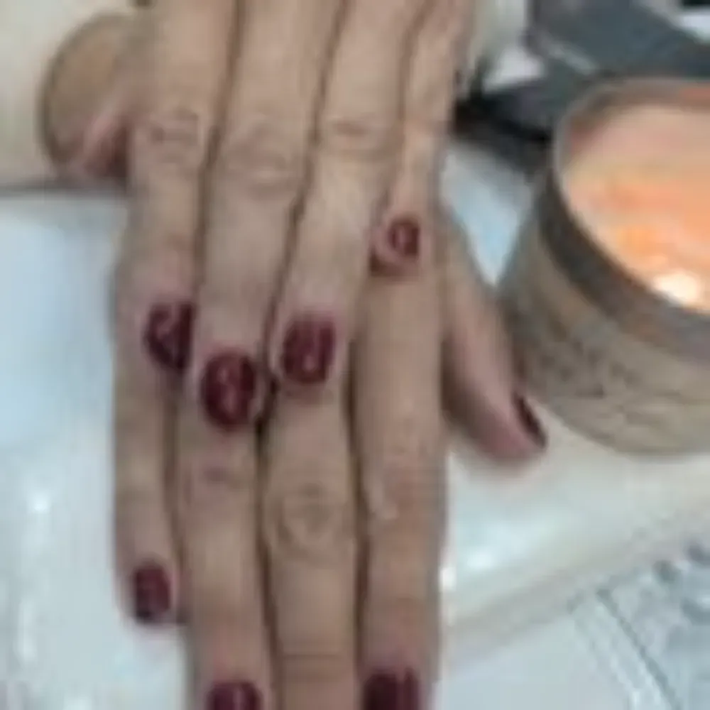 Manos con esmalte de uñas rojo oscuro. Junto a una vela.