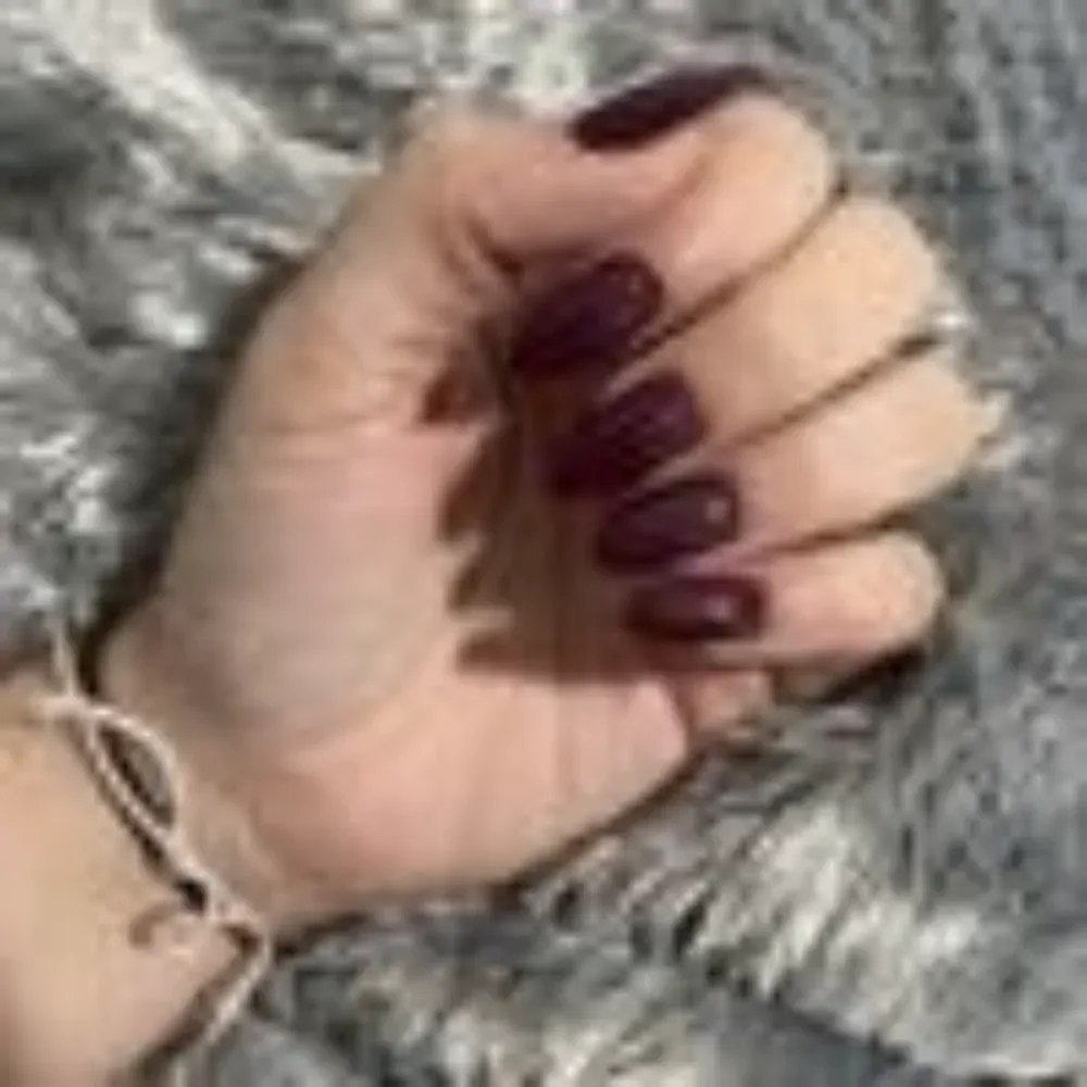 Mano con uñas de color burdeos, puño cerrado sobre superficie gris y esponjosa.