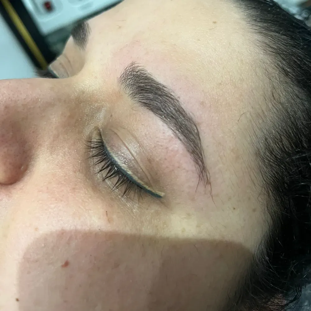 Primer plano del ojo y la ceja de una persona. Ceja oscura con pelos sueltos cerca del inicio. Ojo cerrado, delineador blanco.