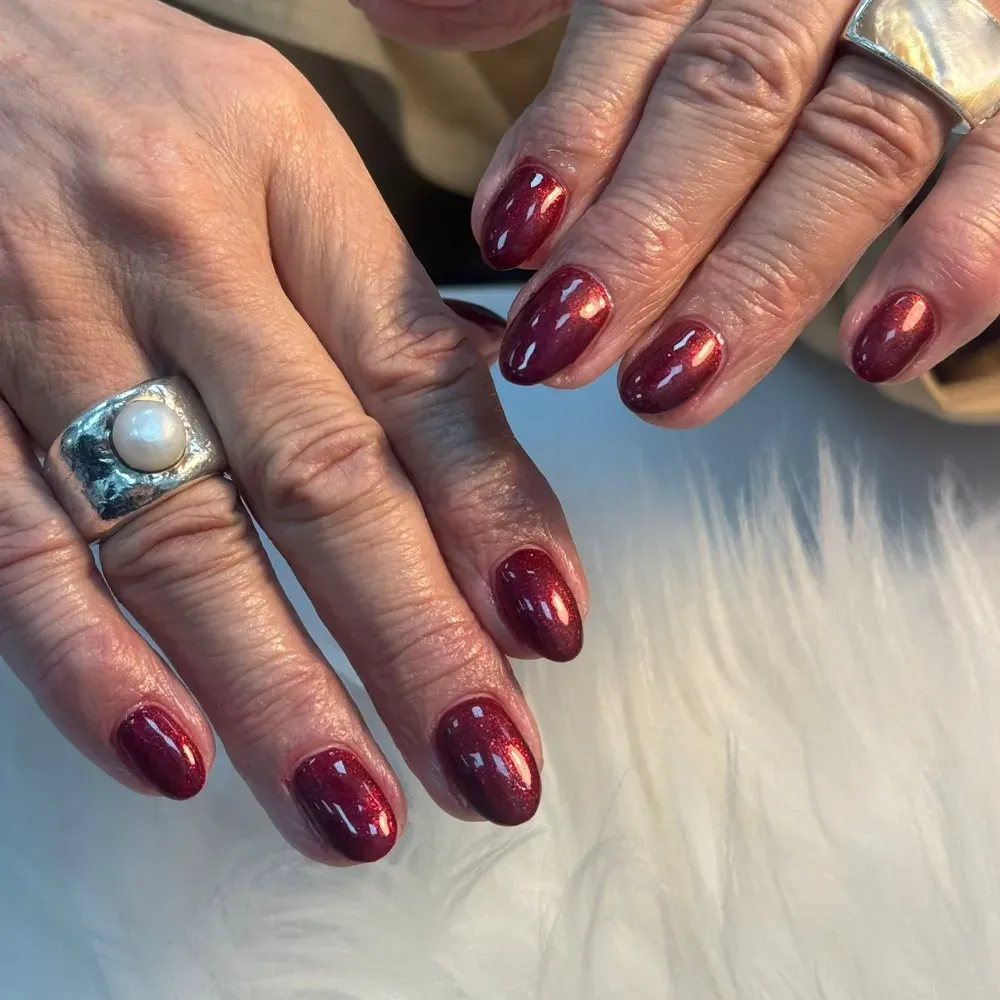 Manos con uñas rojas, pulidas y de forma ovalada, que llevan anillos de plata de gran tamaño.