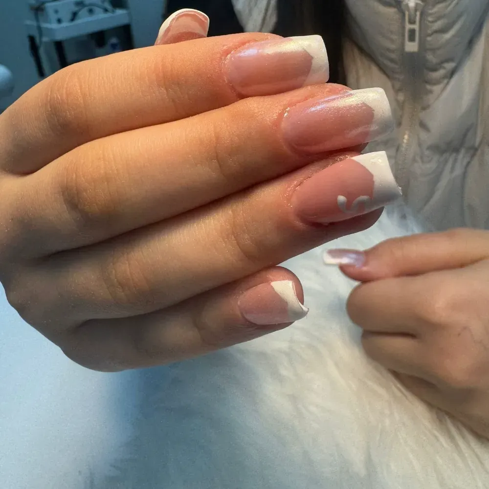 Primer plano de mano con uñas acrílicas de punta francesa, puntas blancas y base transparente.