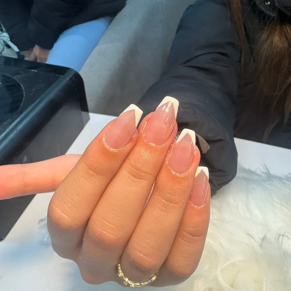 Mano con uñas acrílicas punta francesa y anillo dorado.