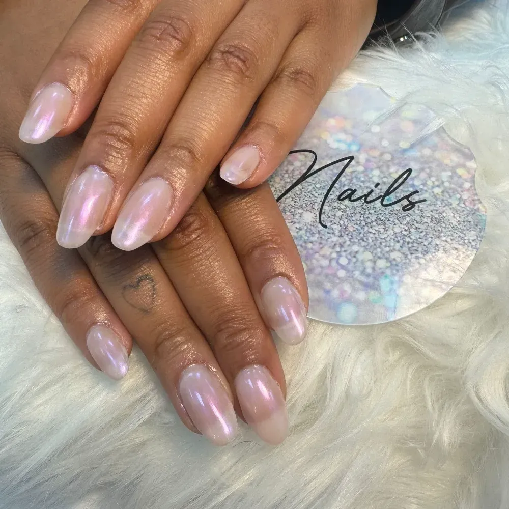 Manos con uñas ovaladas brillantes y perladas; apoyadas sobre una superficie blanca y esponjosa junto a un logotipo 