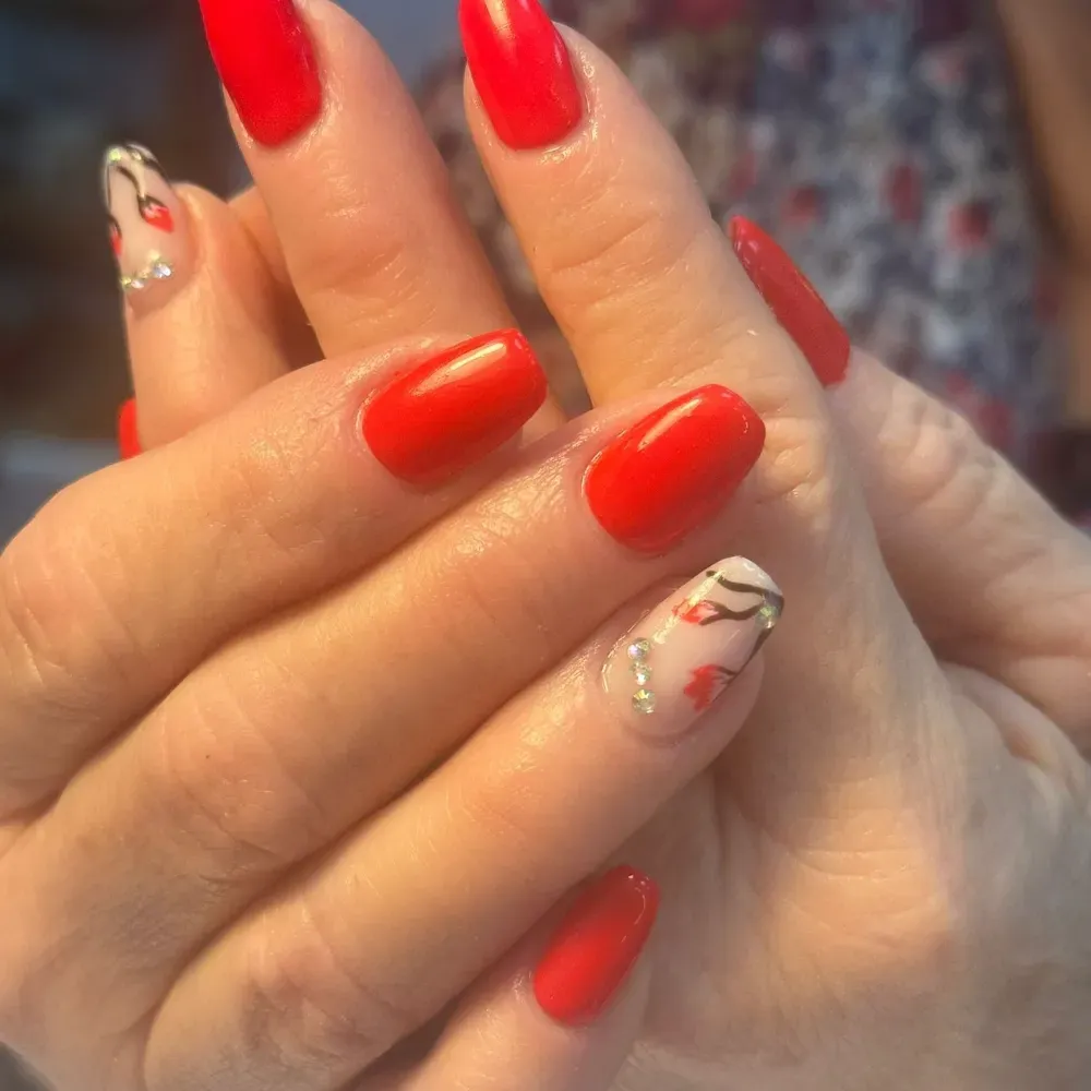 Uñas rojas con dos uñas acentuadas que presentan un diseño con pedrería.