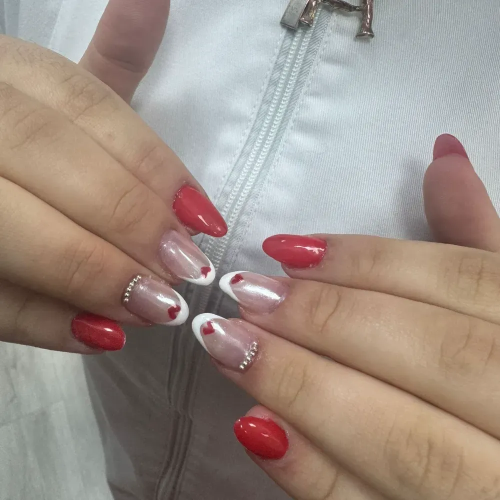 Manos con nail art con temática de corazones rojos y blancos; el fondo es una chaqueta blanca.