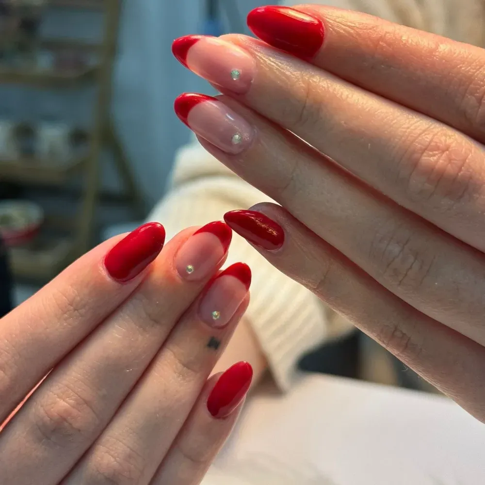 Manos con uñas de punta francesa rojas, algunas con pequeñas gemas.