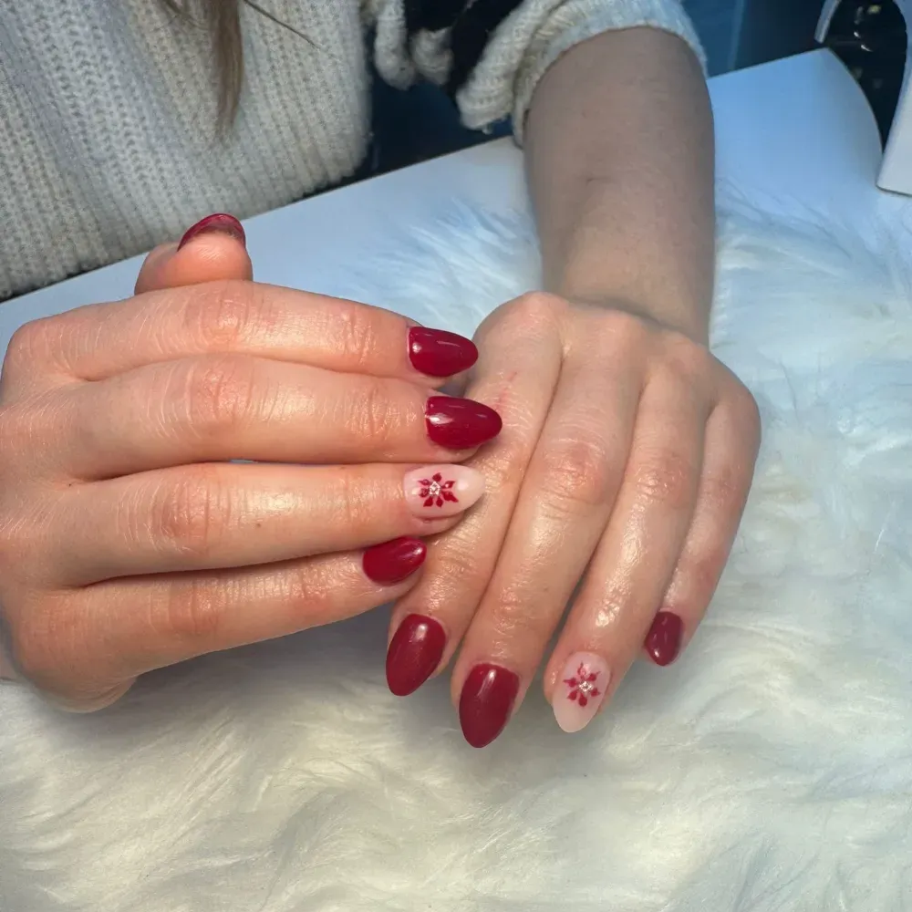 Manos con uñas rojas en forma de almendra, dos de ellas acentuadas con diseños florales, descansando sobre una superficie blanca y esponjosa.