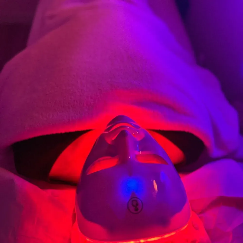 Persona con máscara de fototerapia LED. Rostro iluminado con luces rojas y azules.