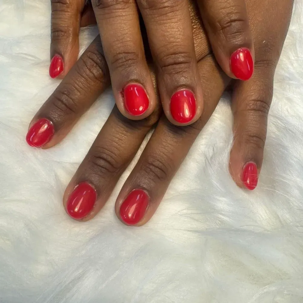 Manos con uñas cortas, redondeadas y rojas, que descansan sobre una superficie blanca y borrosa.