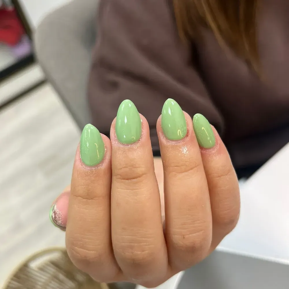 Mano con uñas en forma de almendra pintadas de color verde claro.