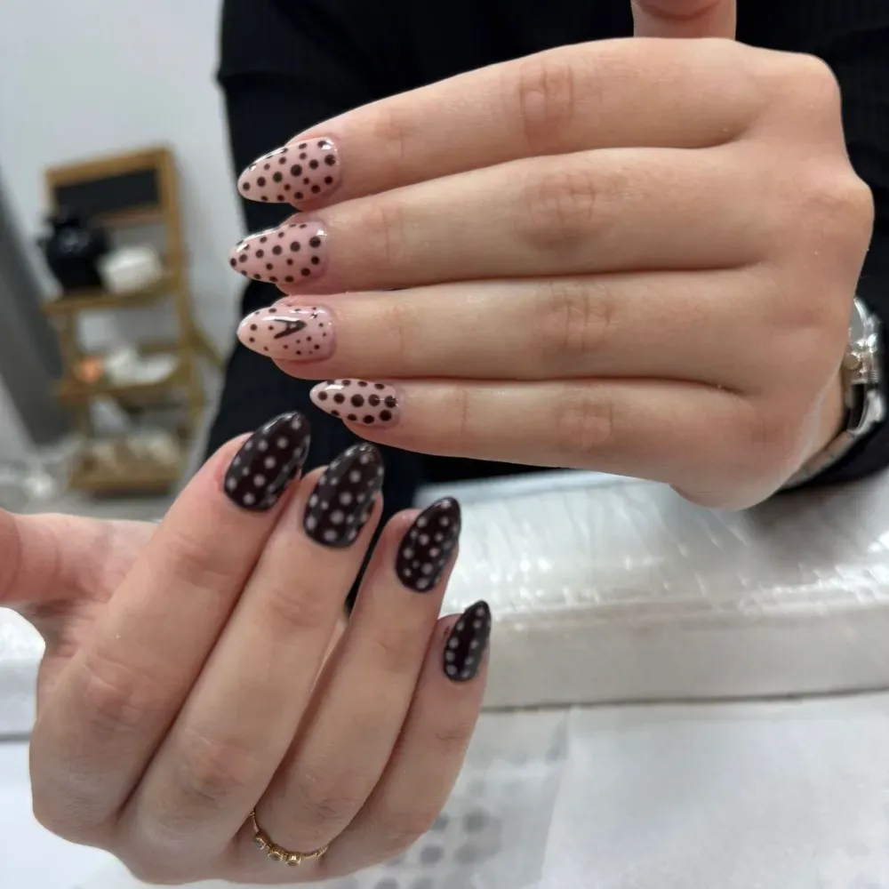Manos con uñas en forma de almendra, algunas color nude con lunares negros, otras color negro liso con lunares.