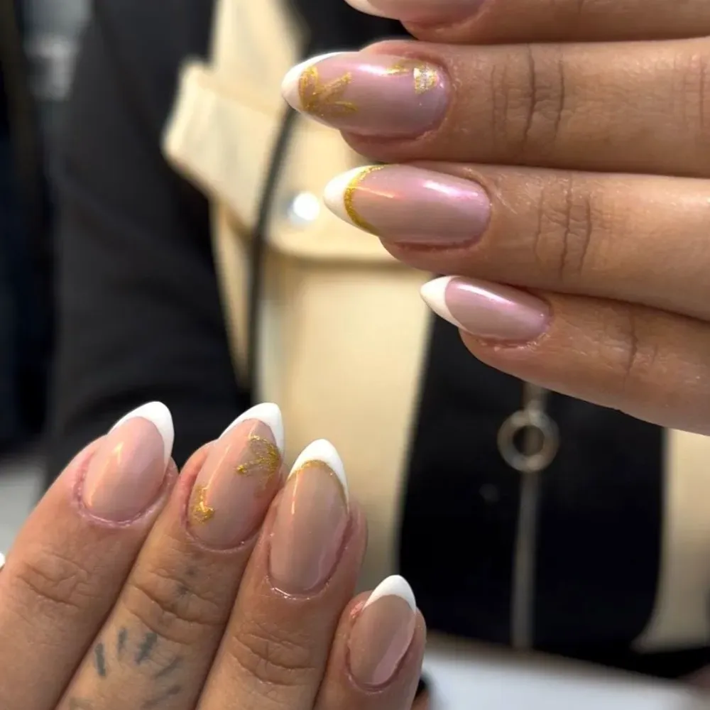 Uñas cuidadas con puntas blancas, detalles dorados y base nude.