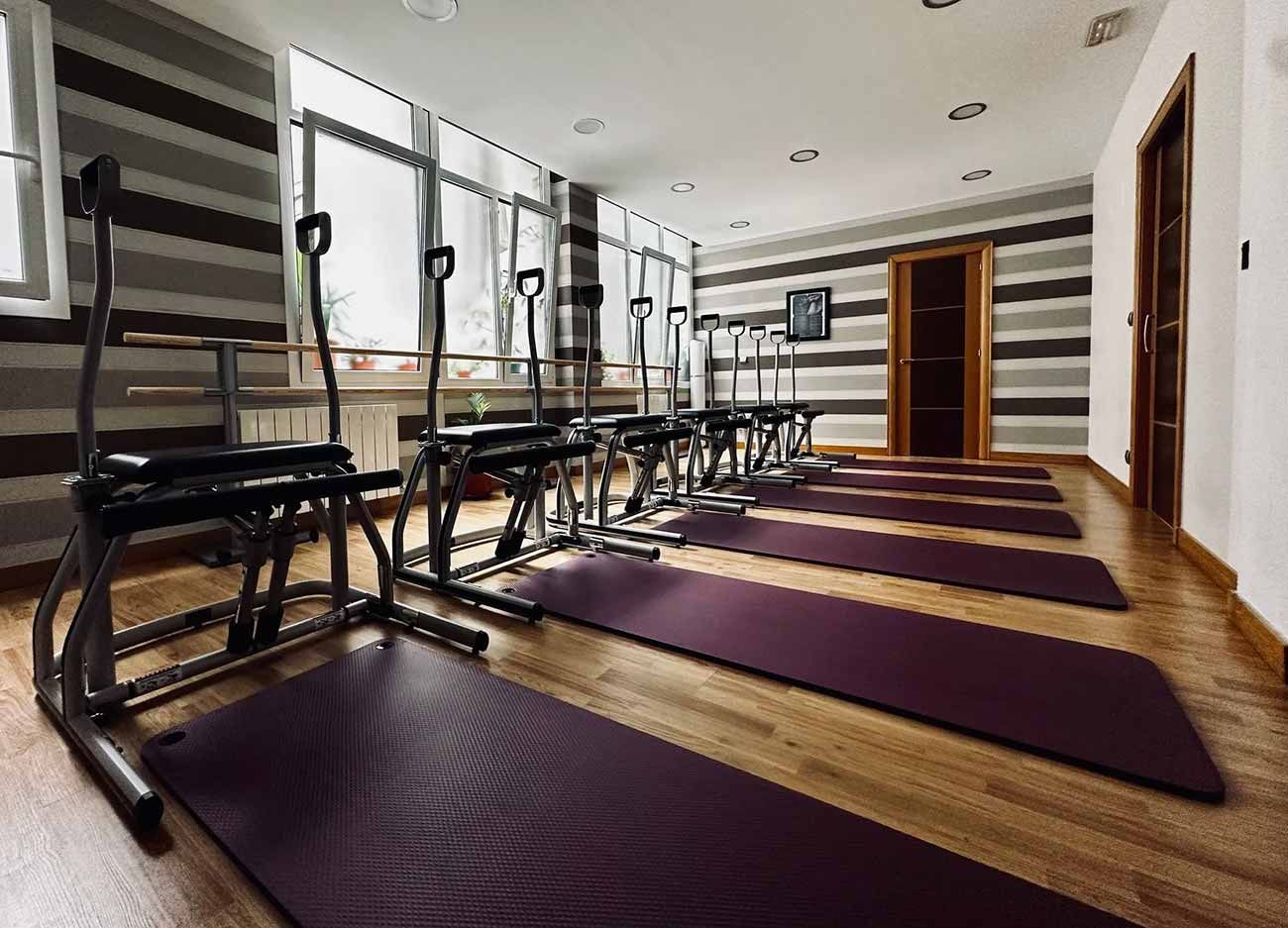 Estudio de Pilates con aparatos de ejercicio, colchonetas moradas y paredes a rayas.