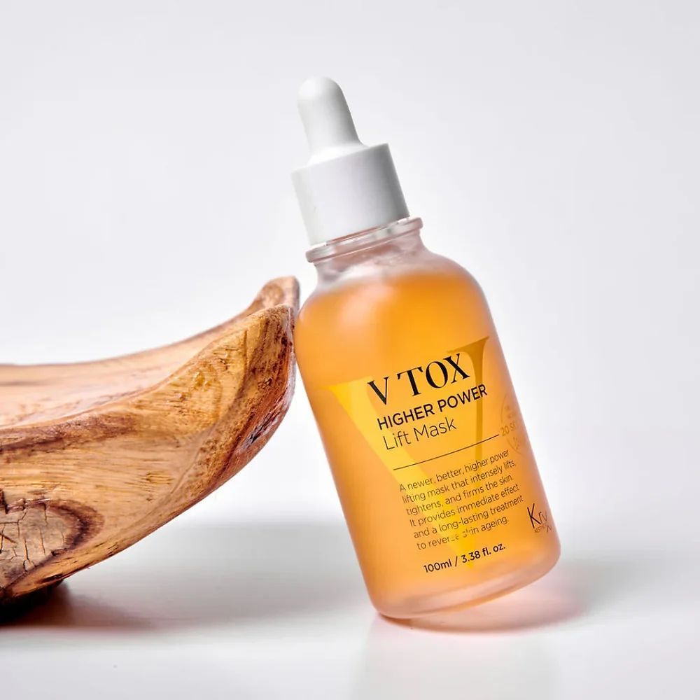 Frasco de sérum facial color ámbar con gotero junto a un cuenco de madera sobre un fondo blanco.