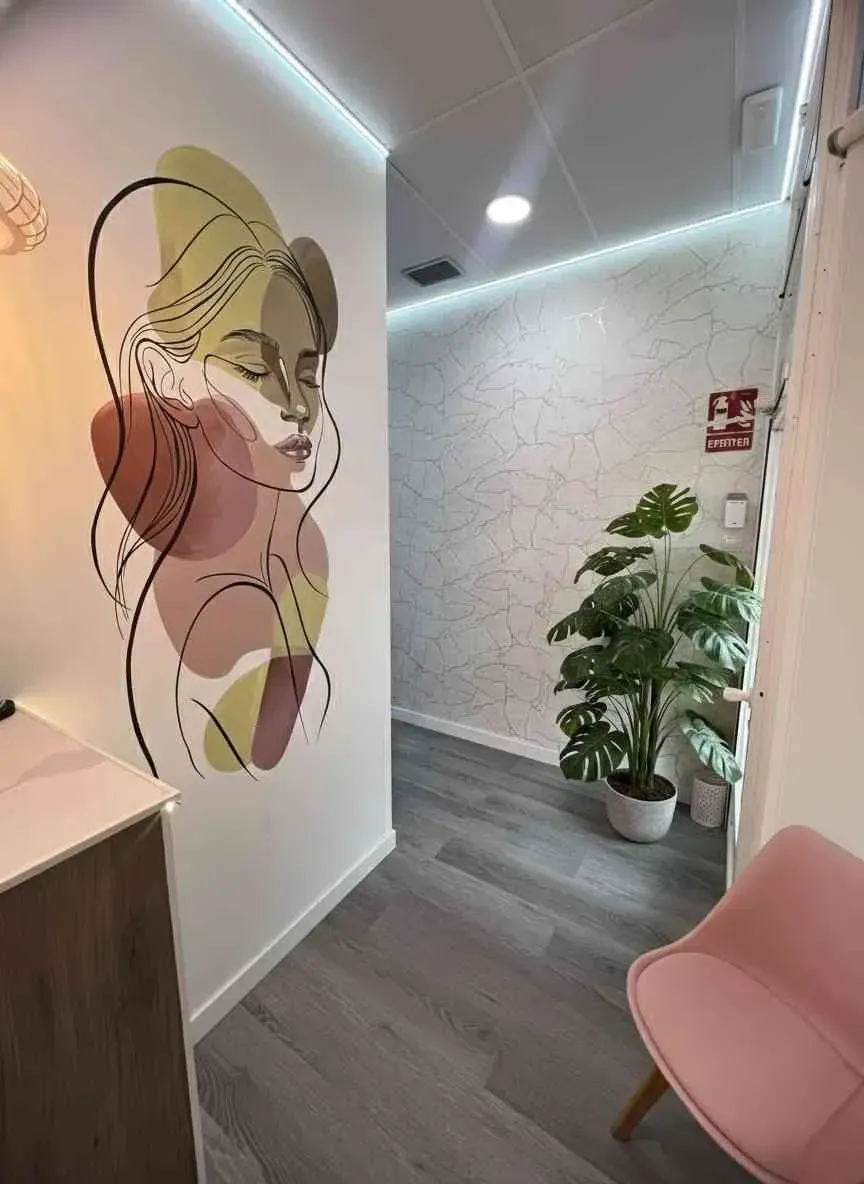 Pasillo con mural de rostro de mujer, suelo gris, silla rosa y planta en maceta.