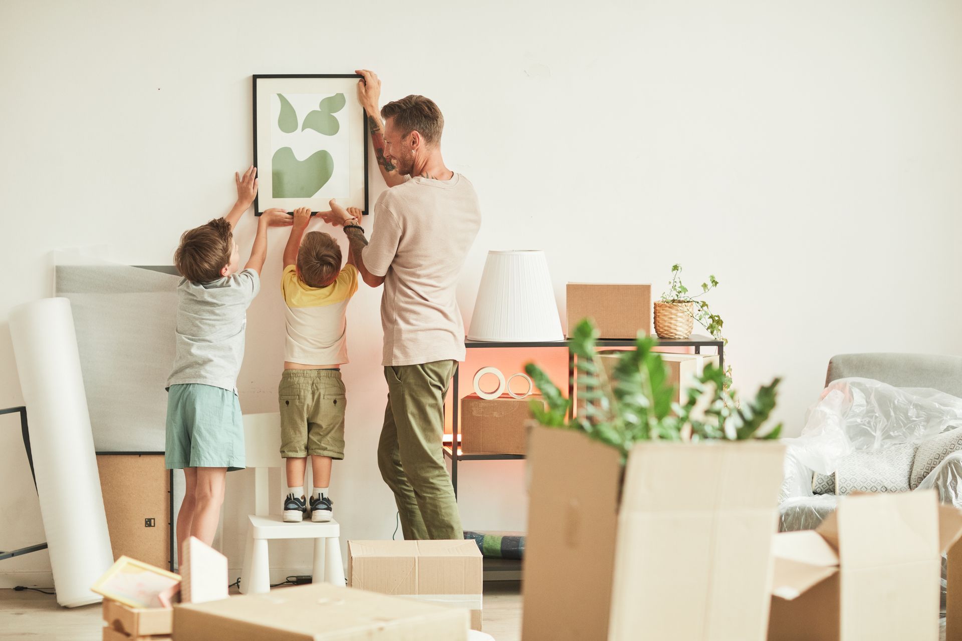 Un homme et deux enfants décrochent un tableau au milieu de cartons de déménagement