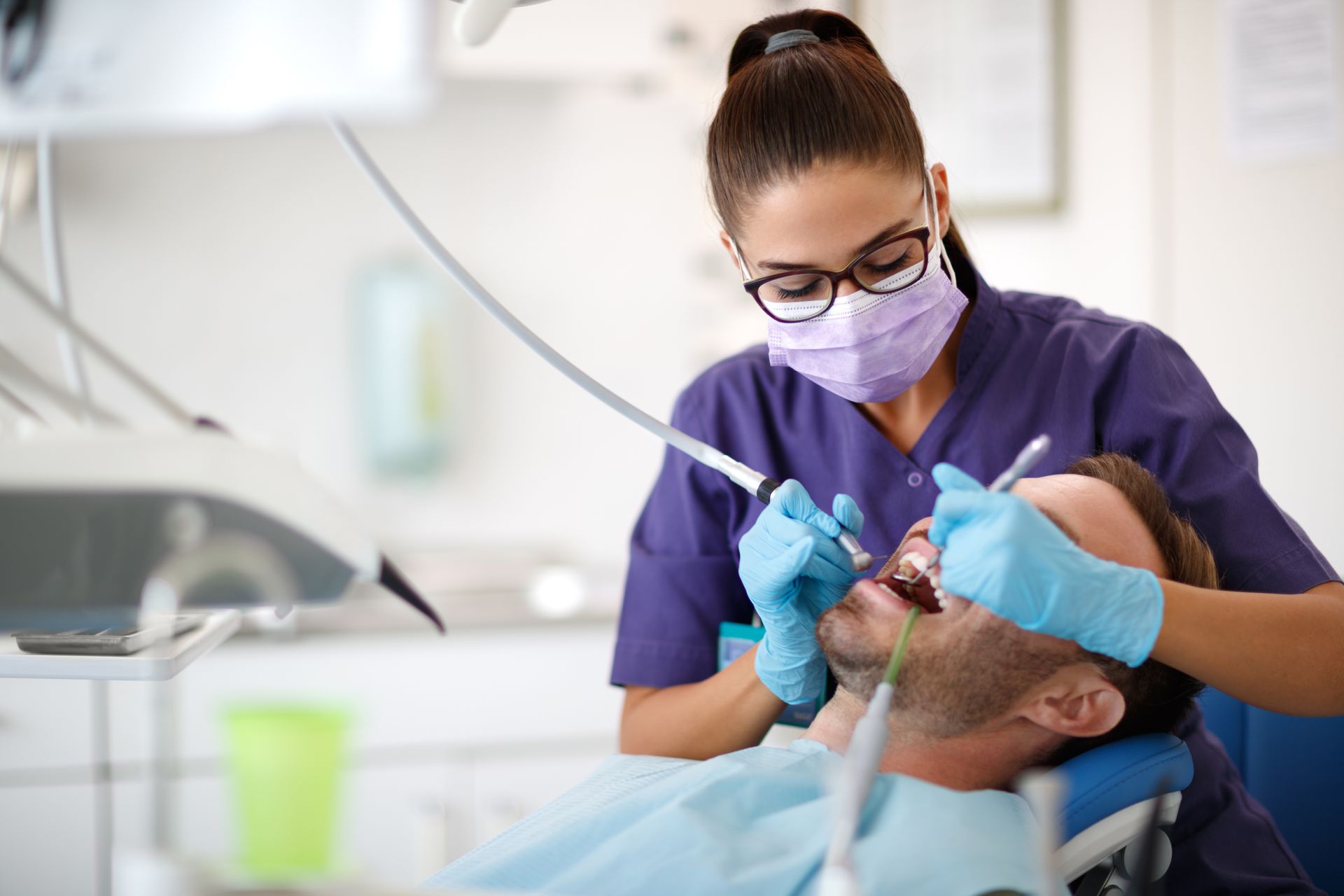 Un dentiste en blouse et masque violets soigne un patient allongé dans une clinique dentaire lumineuse.