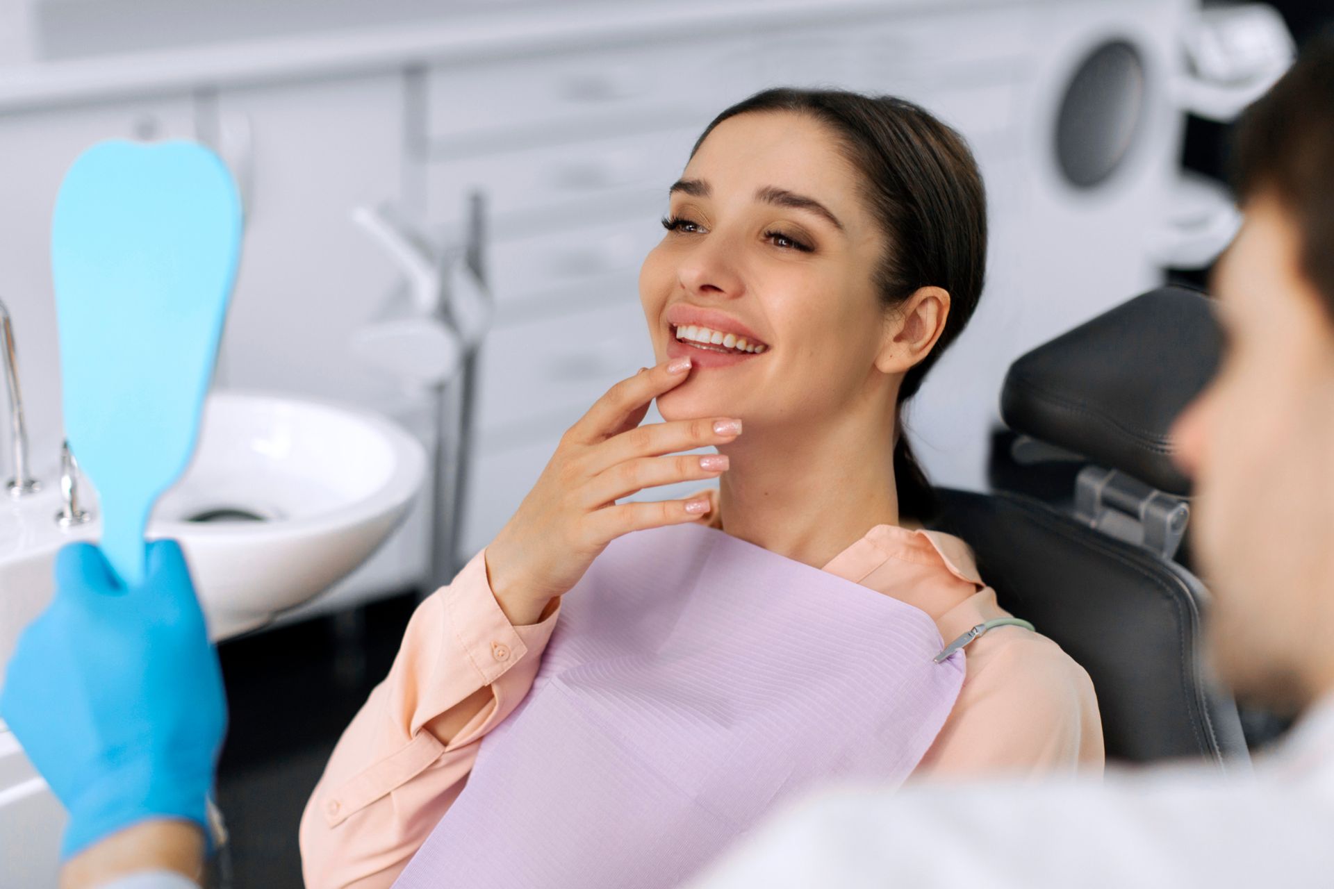 Une femme assise sur un fauteuil de dentiste sourit tandis qu'un dentiste tient un miroir, un instrument dentaire bleu se trouvant à proximité.