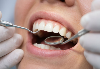Un dentiste examine les dents d'un patient à l'aide d'un miroir et d'instruments dentaires.