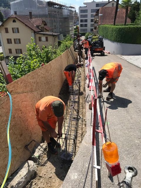 Bauarbeiter in orangefarbenen Westen errichten eine Mauer; Strasse mit Absperrungen und Beleuchtung abgesperrt.