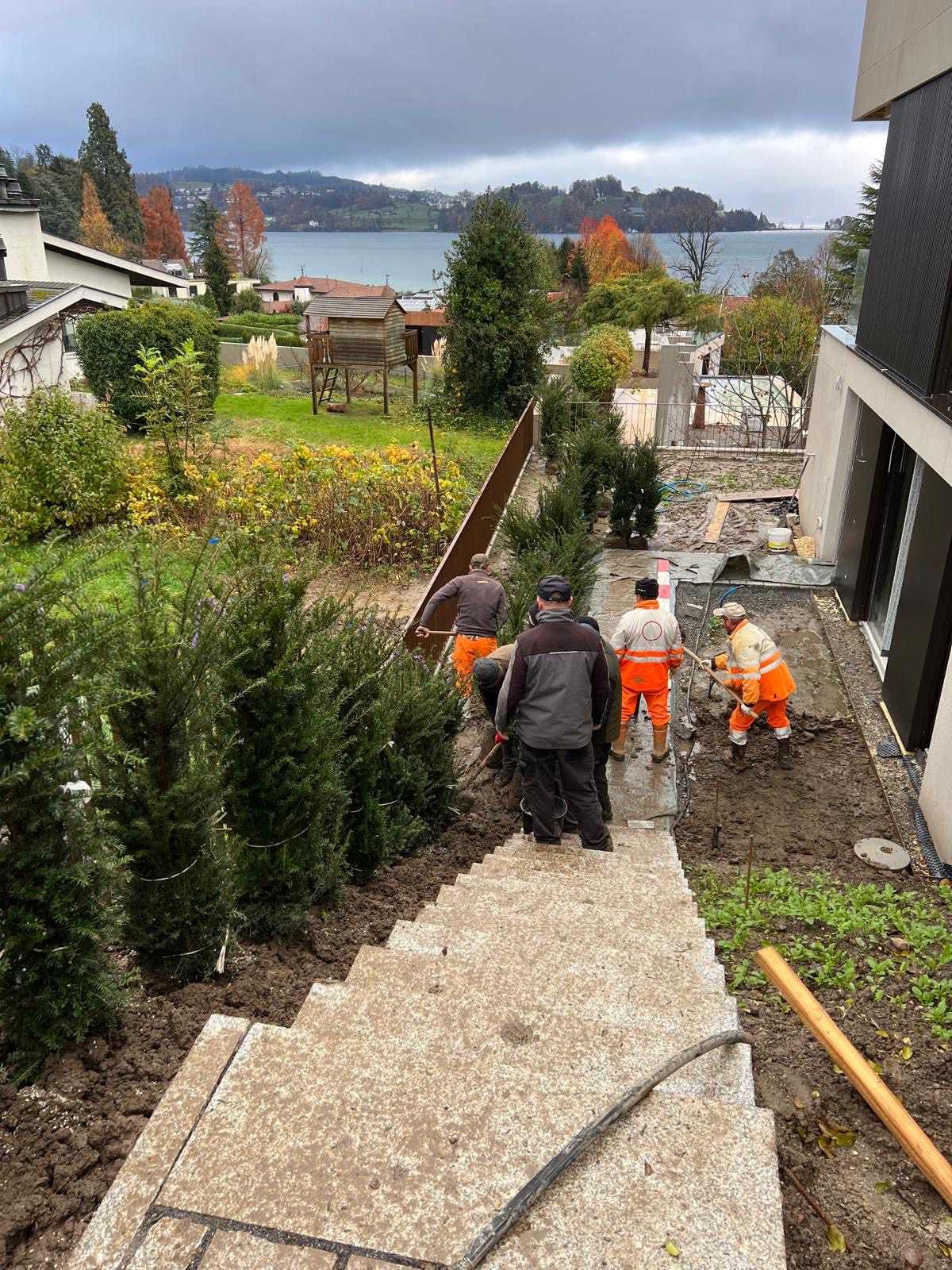 Bauarbeiter in orangefarbenen Westen arbeiten an der Landschaftsgestaltung in der Nähe von Steintreppen und einem See.